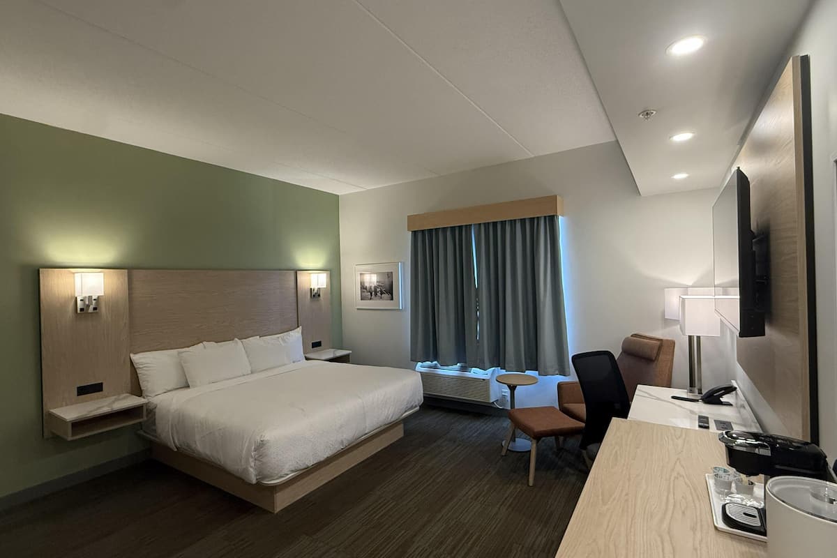 A hotel room with a bed, bedside tables, a desk, a chair, a TV, and a window with curtains.