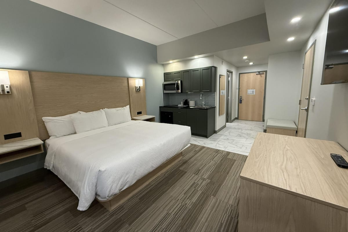 A hotel room with a bed, bedside tables, a desk, a microwave, a sink, and a wardrobe.