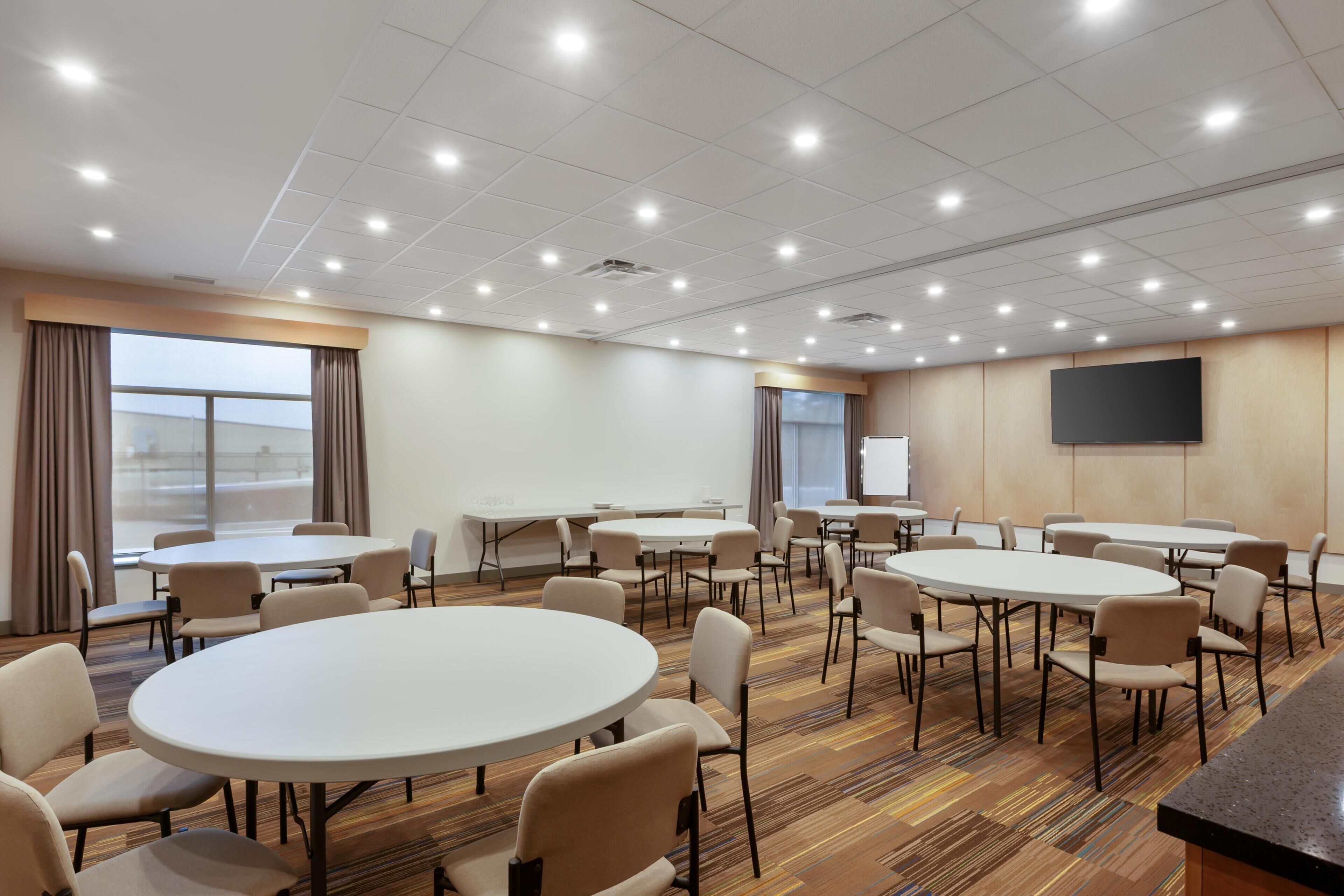 Une salle de conférence dotée de plusieurs tables et chaises, d’un grand écran et d’un sol recouvert de moquette.