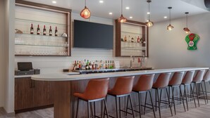 Un espace bar doté d’un long comptoir, de nombreux tabourets et d’étagères remplies de bouteilles et de verres.