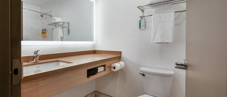 A modern bathroom with a wooden vanity, a large mirror, a toilet, and a towel rack.