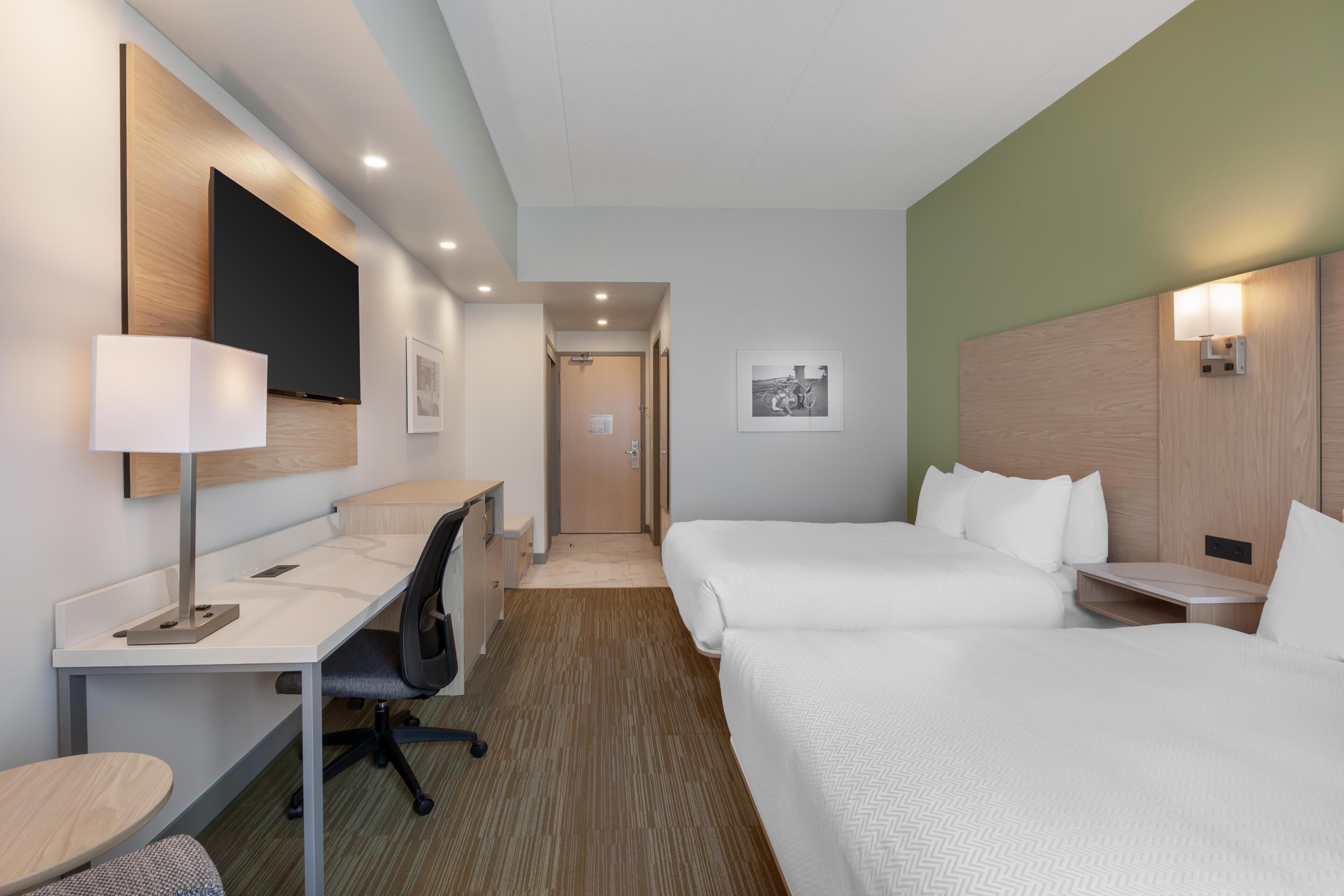 Une chambre d’hôtel équipée d’un bureau, de deux lits, d’une chaise, d’une lampe et d’un tableau encadré au mur.