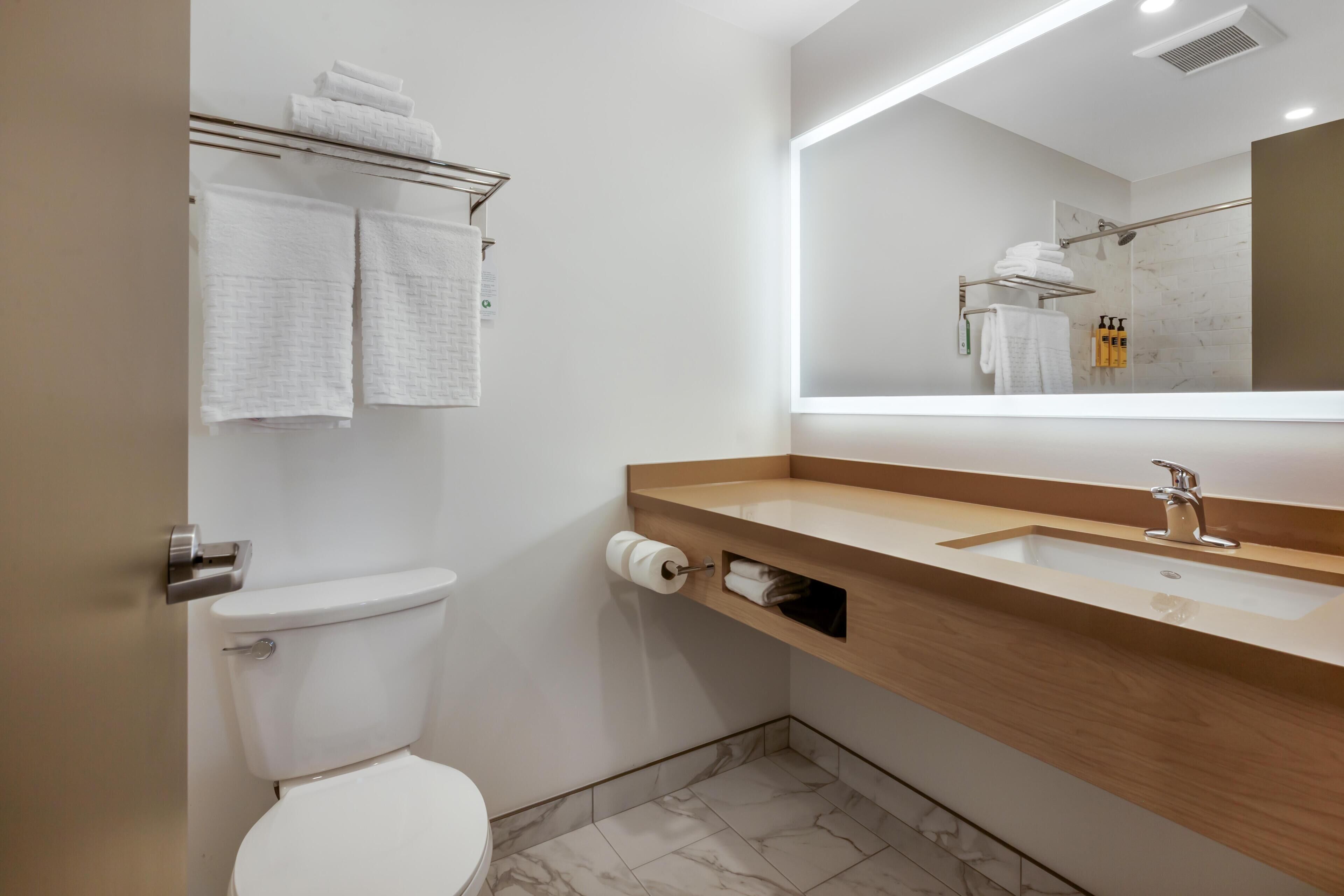 A modern bathroom with a toilet, sink, mirror, and towel rack.