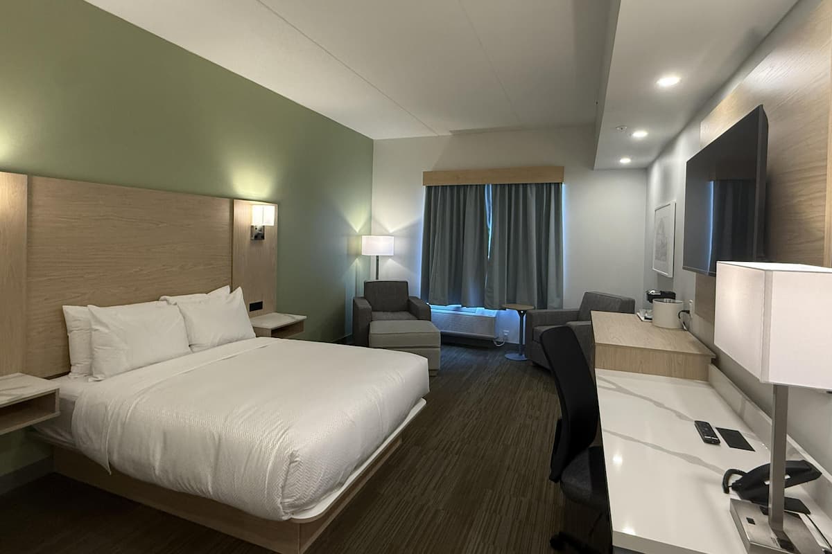 A hotel room with a bed, desk, chair, and a large mirror.