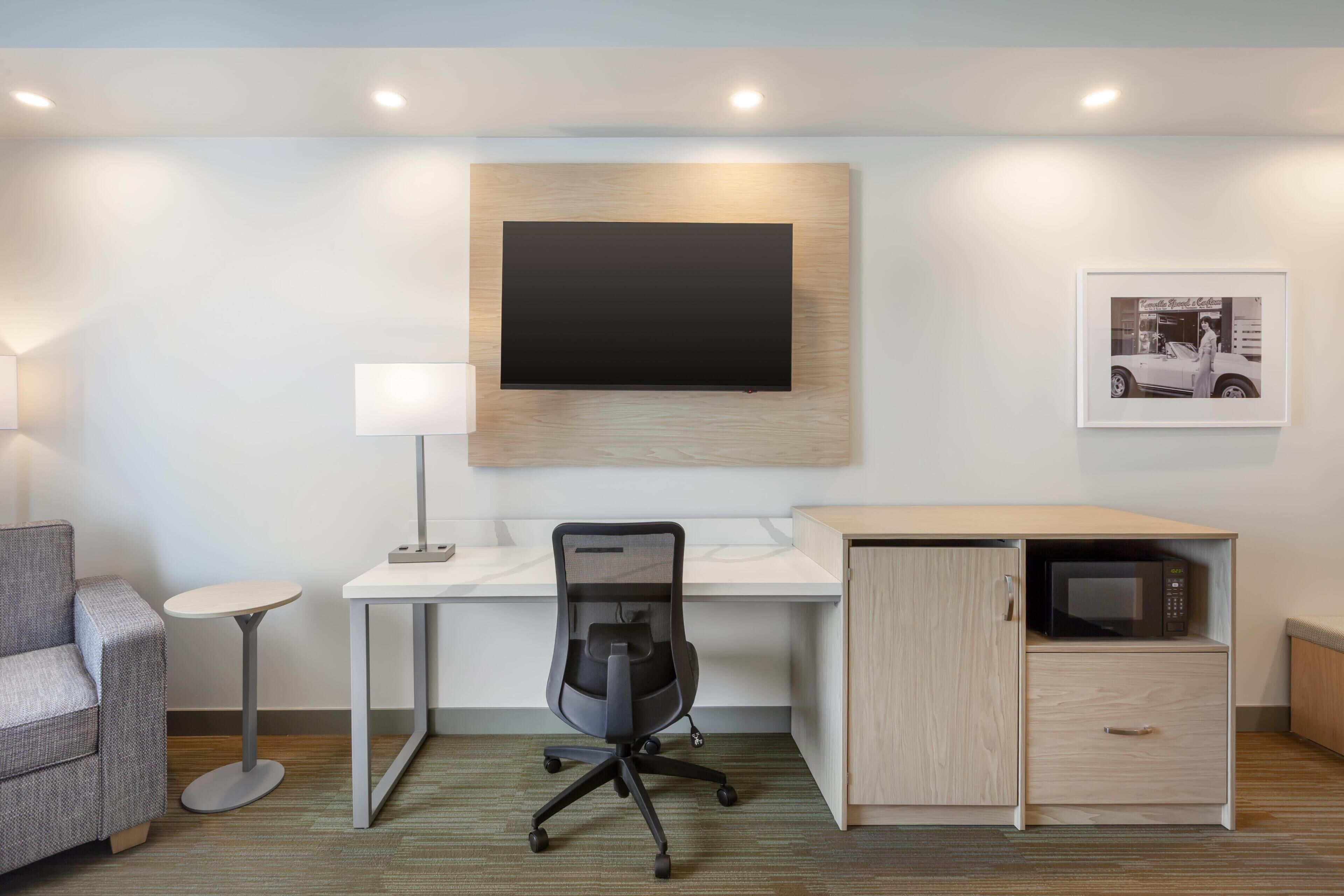 A modern office space with a desk, chair, lamp, and a mounted flat-screen TV.