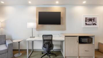 A modern office space with a desk, chair, lamp, and a mounted flat-screen TV.