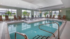 Une piscine dotée de chaises longues et d’une zone peu profonde, le tout entouré de grandes fenêtres.