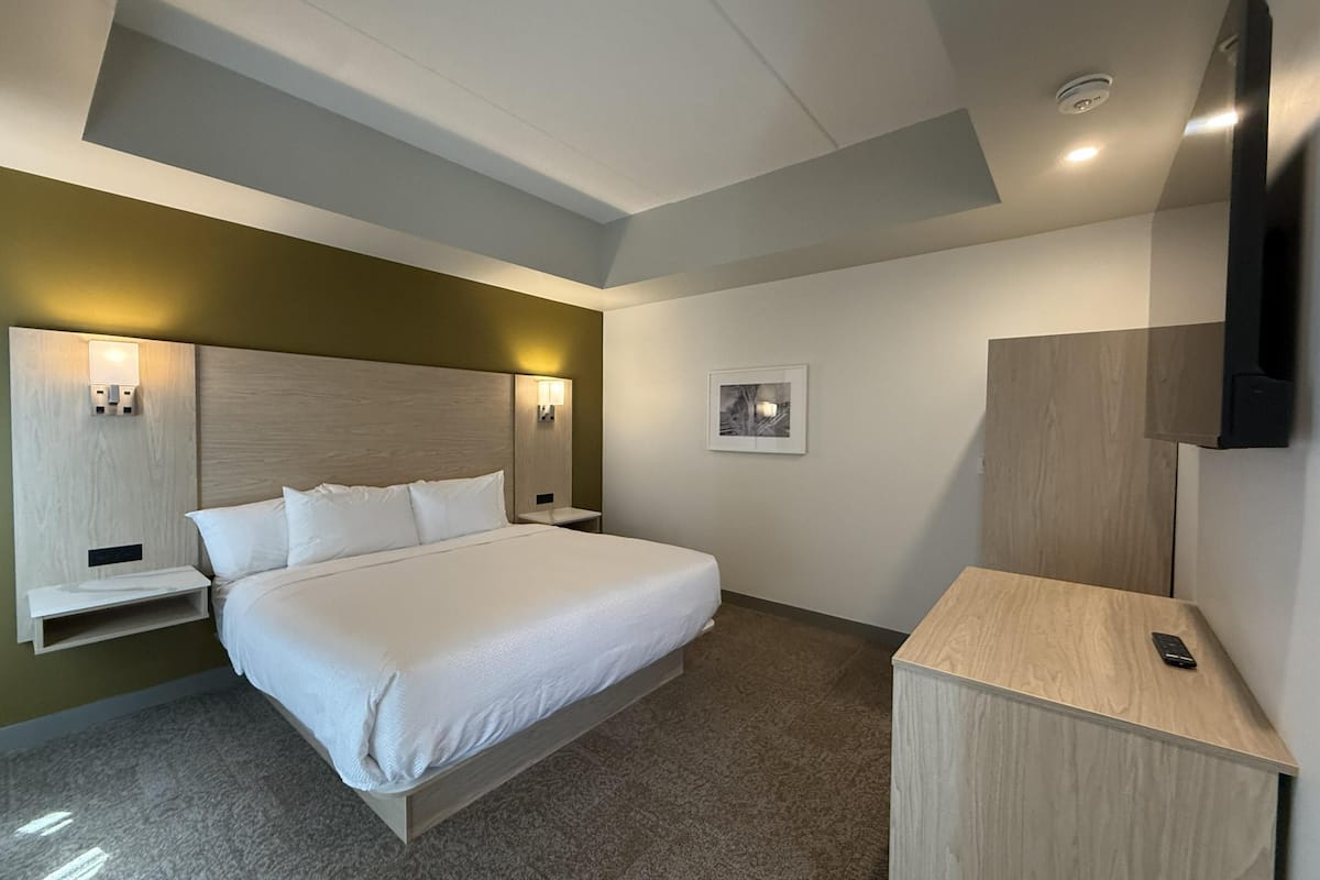 A hotel room with a bed, bedside tables, a wall-mounted TV, and a framed picture on the wall.