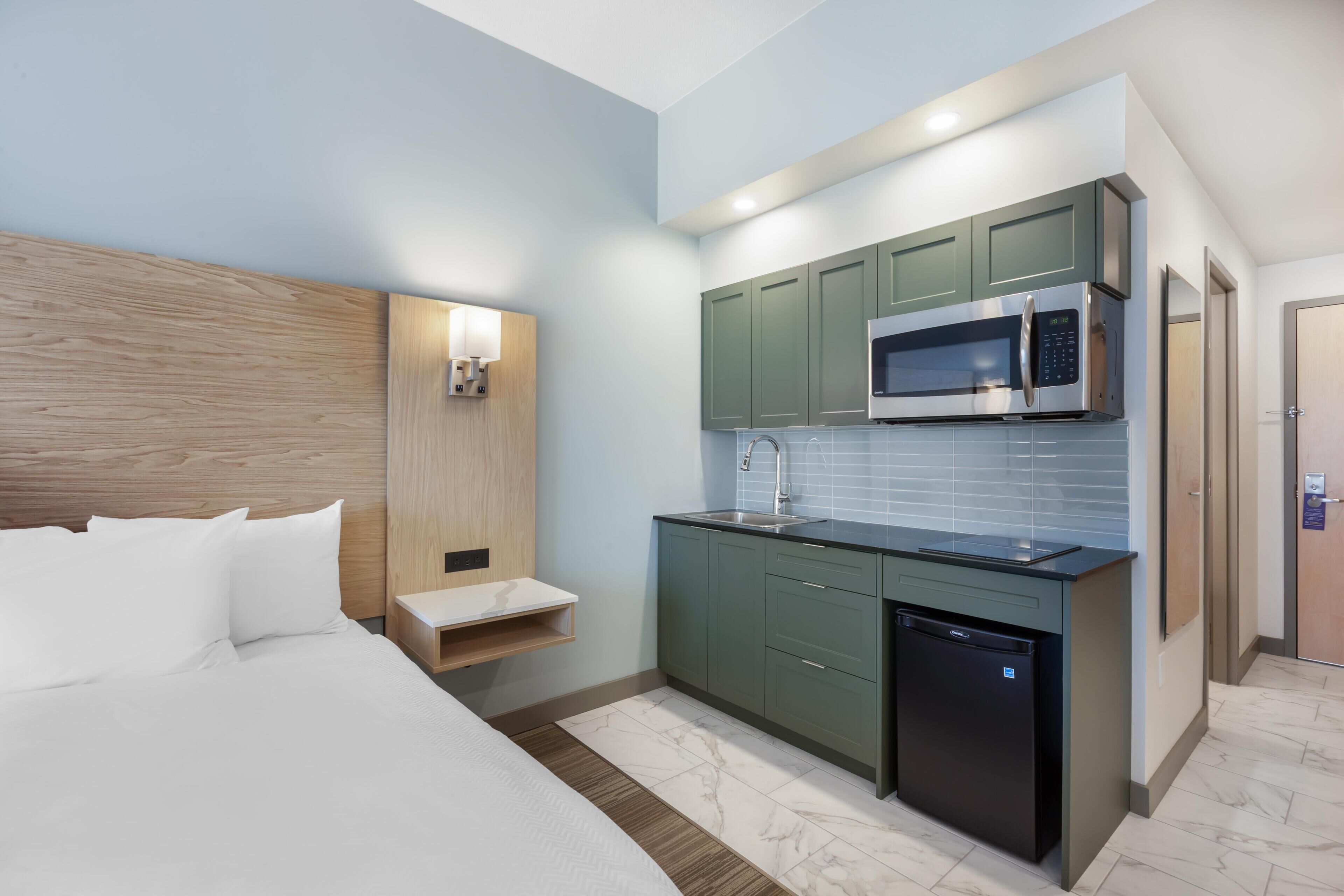 Une chambre d’hôtel moderne équipée d’un lit, d’une petite kitchenette avec un four à micro-ondes, un évier et un lave-vaisselle.