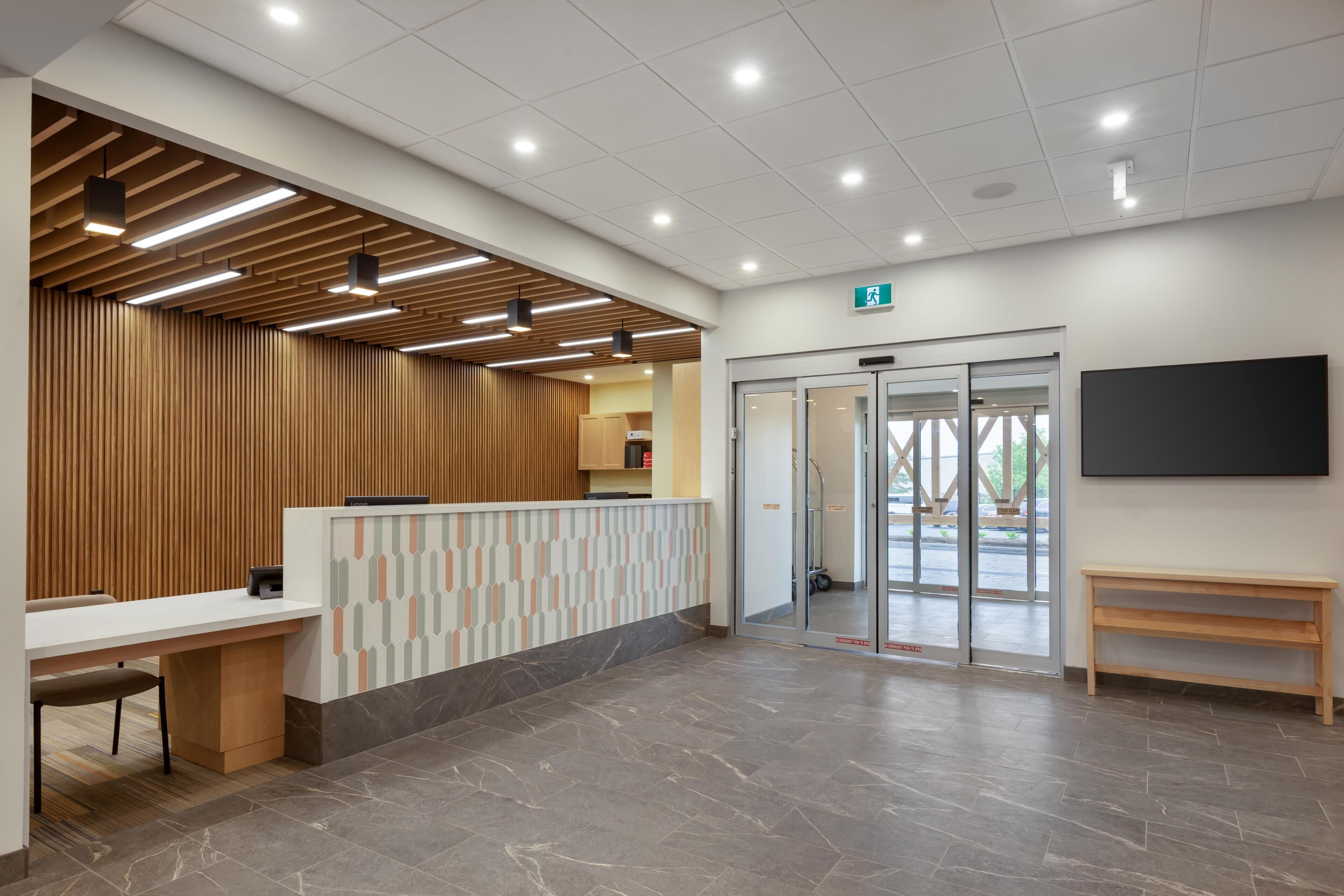 A reception area with a reception desk, a wooden panel wall, a patterned wall, a bench, and a door leading outside.