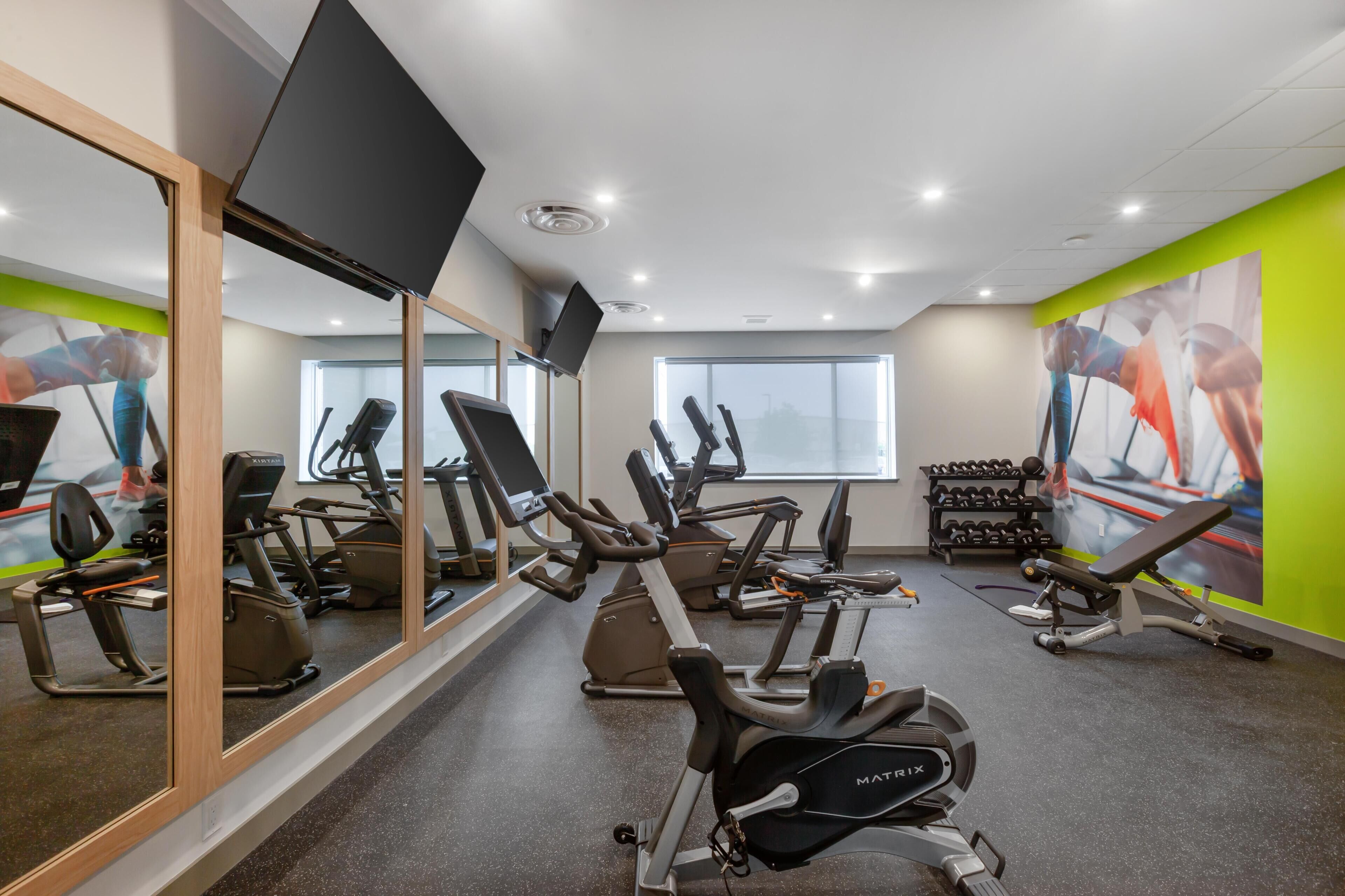 A gym with cardio machines, a mirror, and a window.