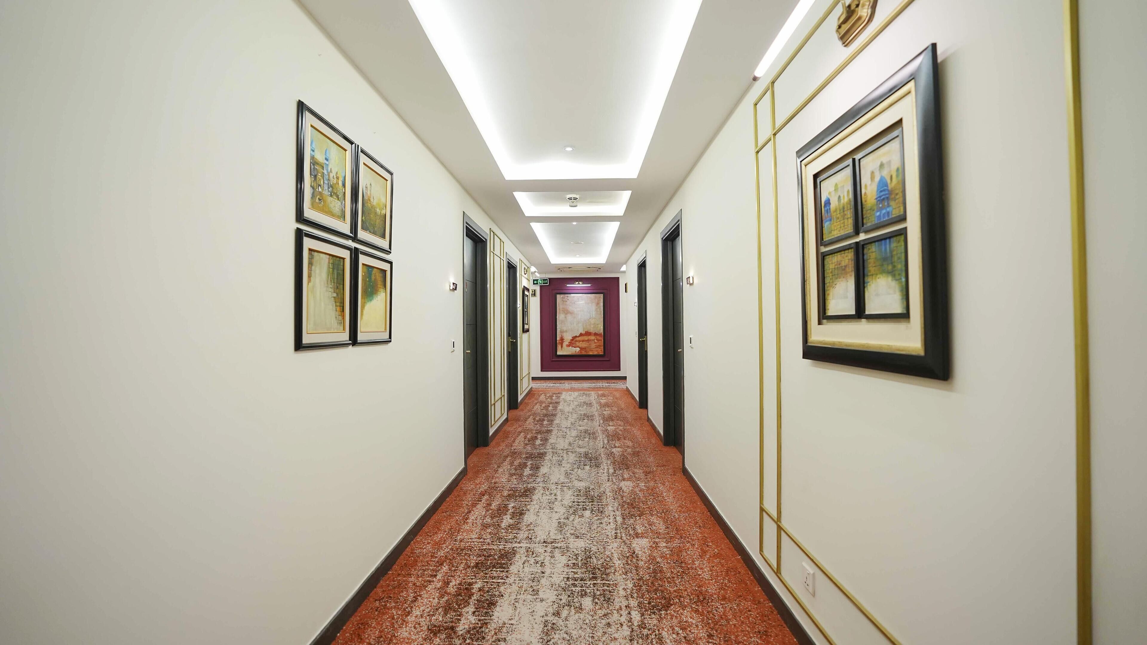 A hotel hallway with framed artwork on the walls, a patterned carpet, and a ceiling light.