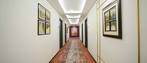 A hotel hallway with framed artwork on the walls, a patterned carpet, and a ceiling light.