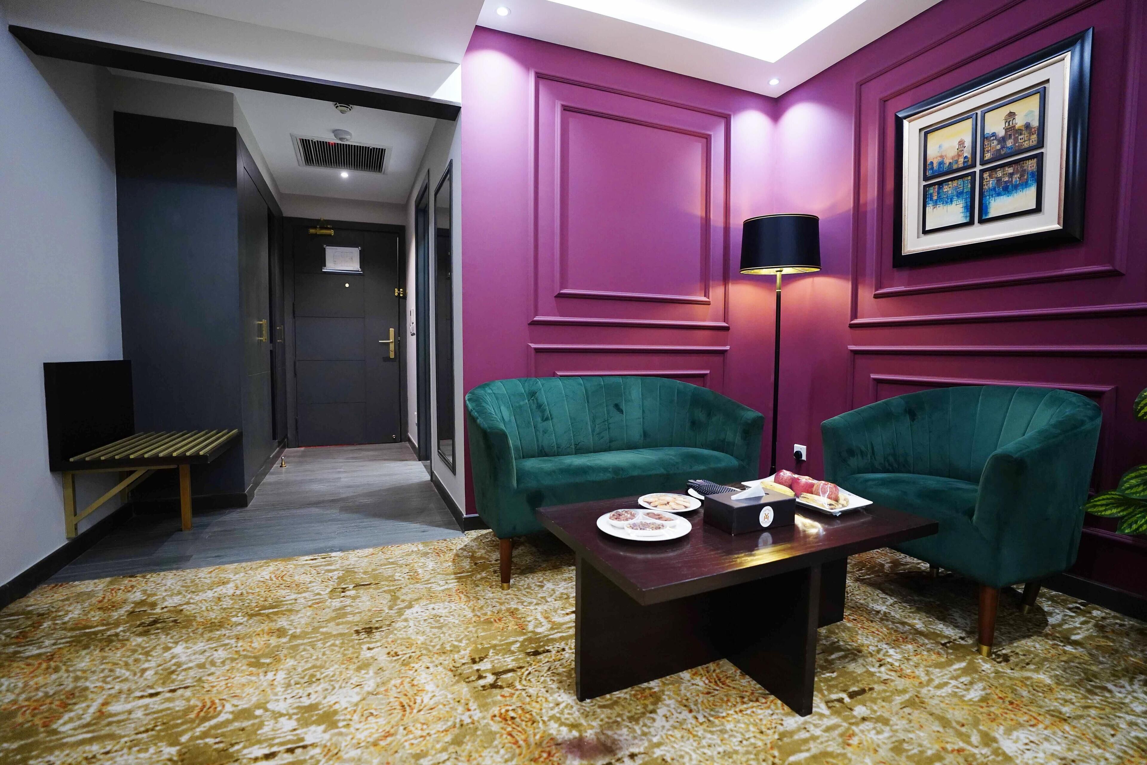 Ein Zimmer mit violetten Wänden, einem grünen Sofa, einem kleinen Tisch mit einer Lampe und einem gerahmten Bild an der Wand.