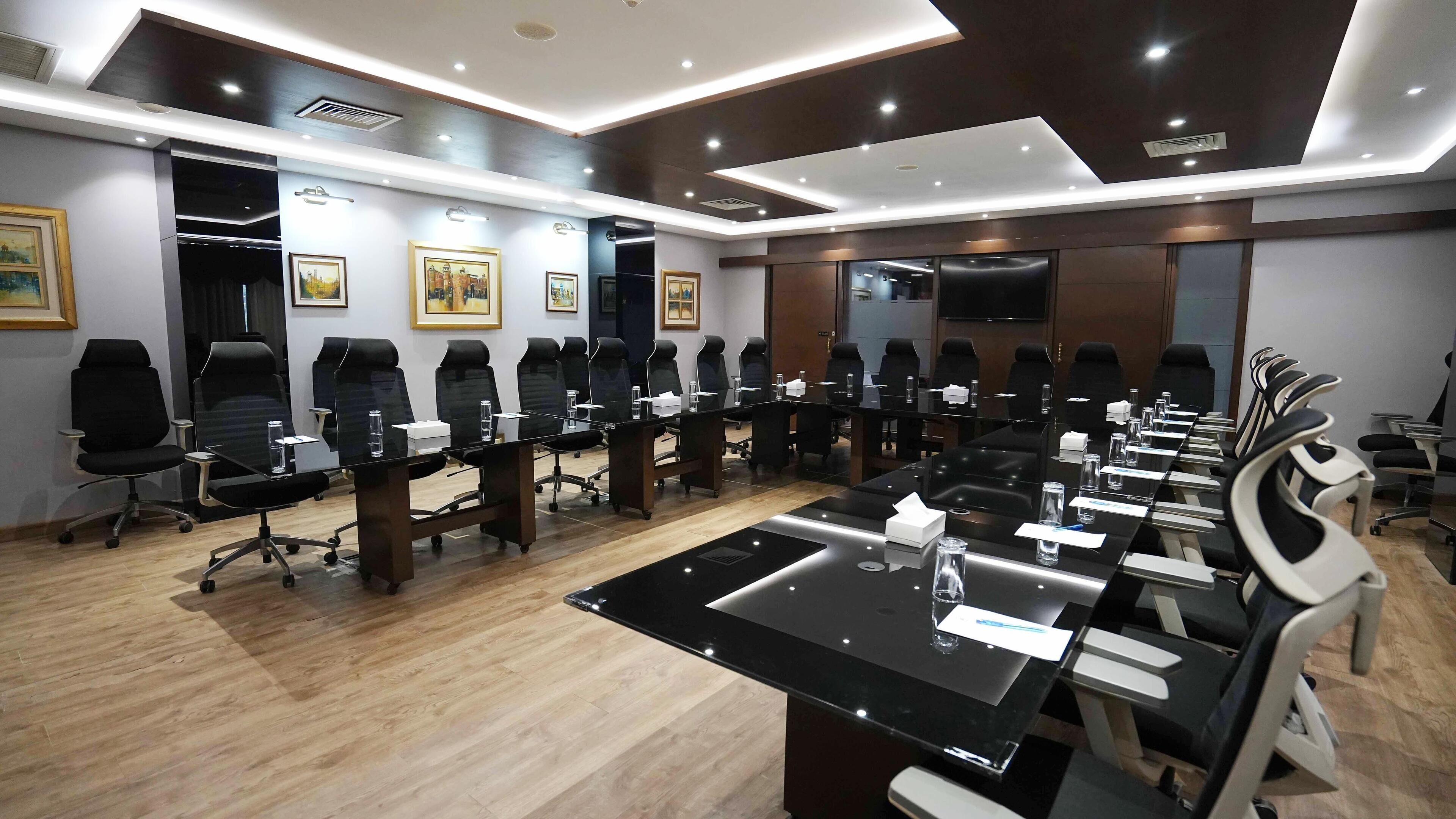 A conference room with multiple black chairs around a central table, equipped with water bottles and tissues.