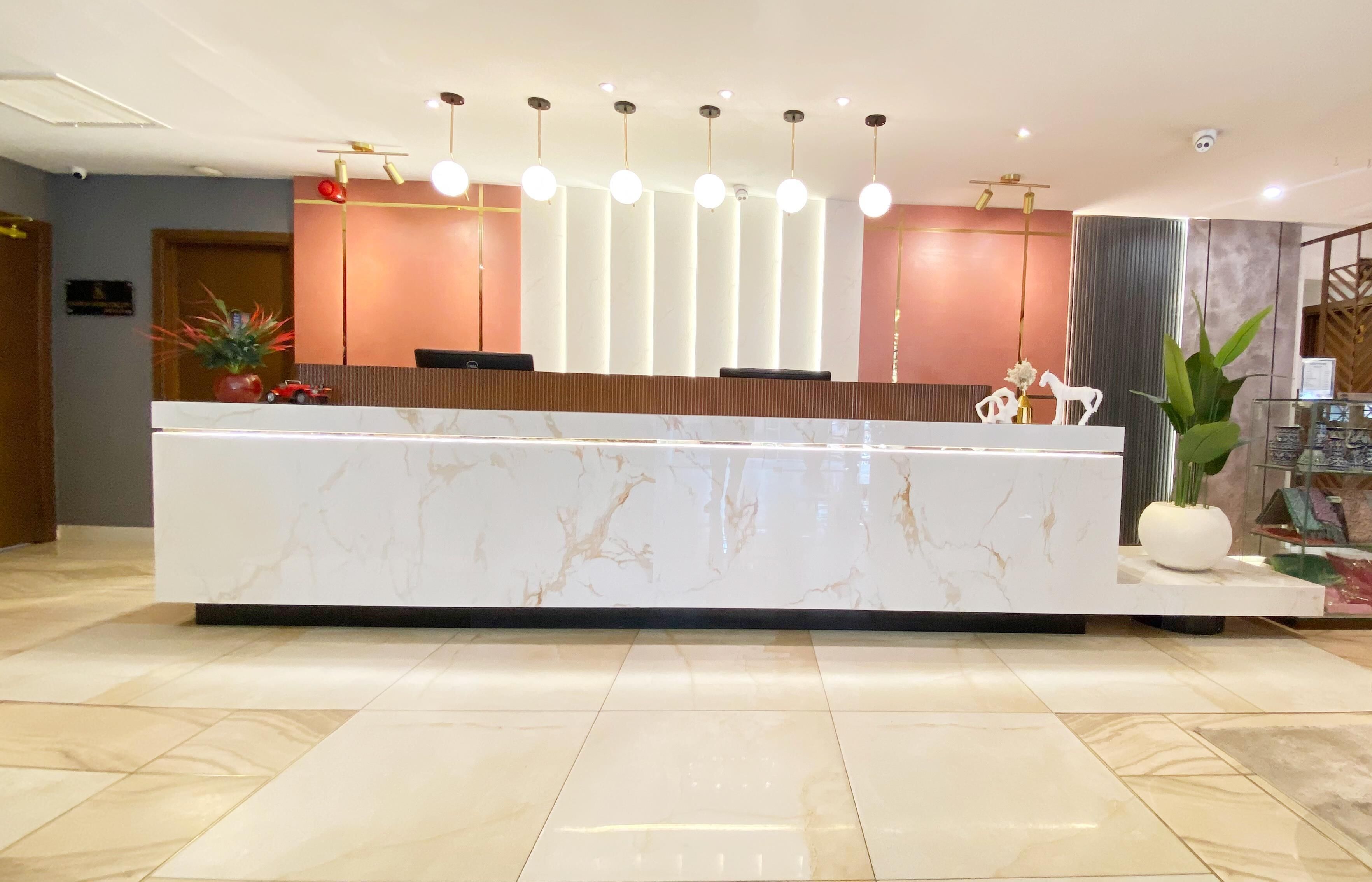 A reception desk with a marble top, a modern light fixture, and a potted plant.