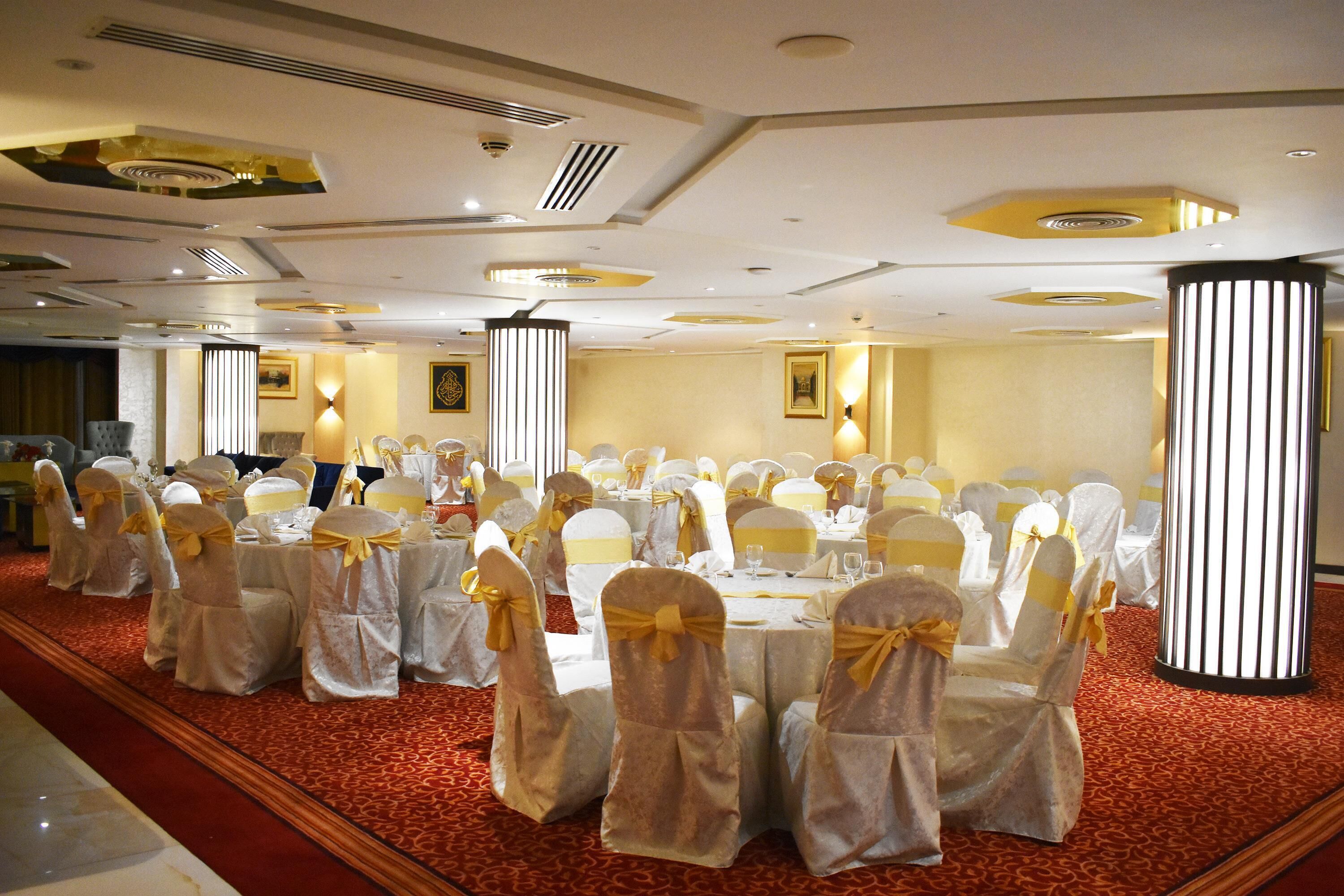 Une salle de banquet avec des tables rondes, des chaises ornées de rubans dorés et un éclairage décoratif.