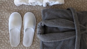 A bed with a patterned bedspread, two pairs of slippers, and a folded bathrobe.