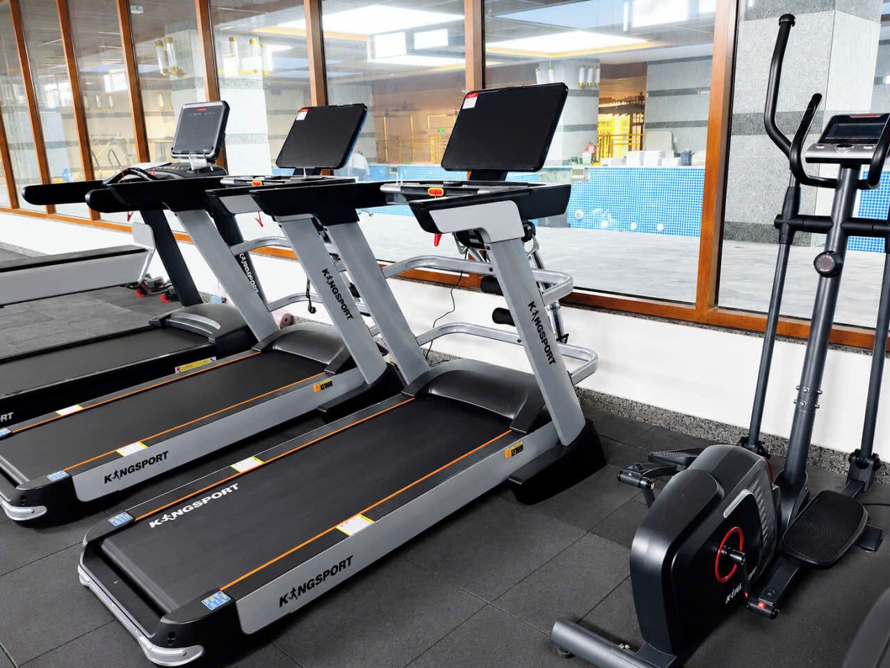 Tres cintas de correr KINGSPOINT en un gimnasio con vista a una piscina a través de grandes ventanales.