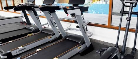 Tres cintas de correr KINGSPOINT en un gimnasio con vista a una piscina a través de grandes ventanales.
