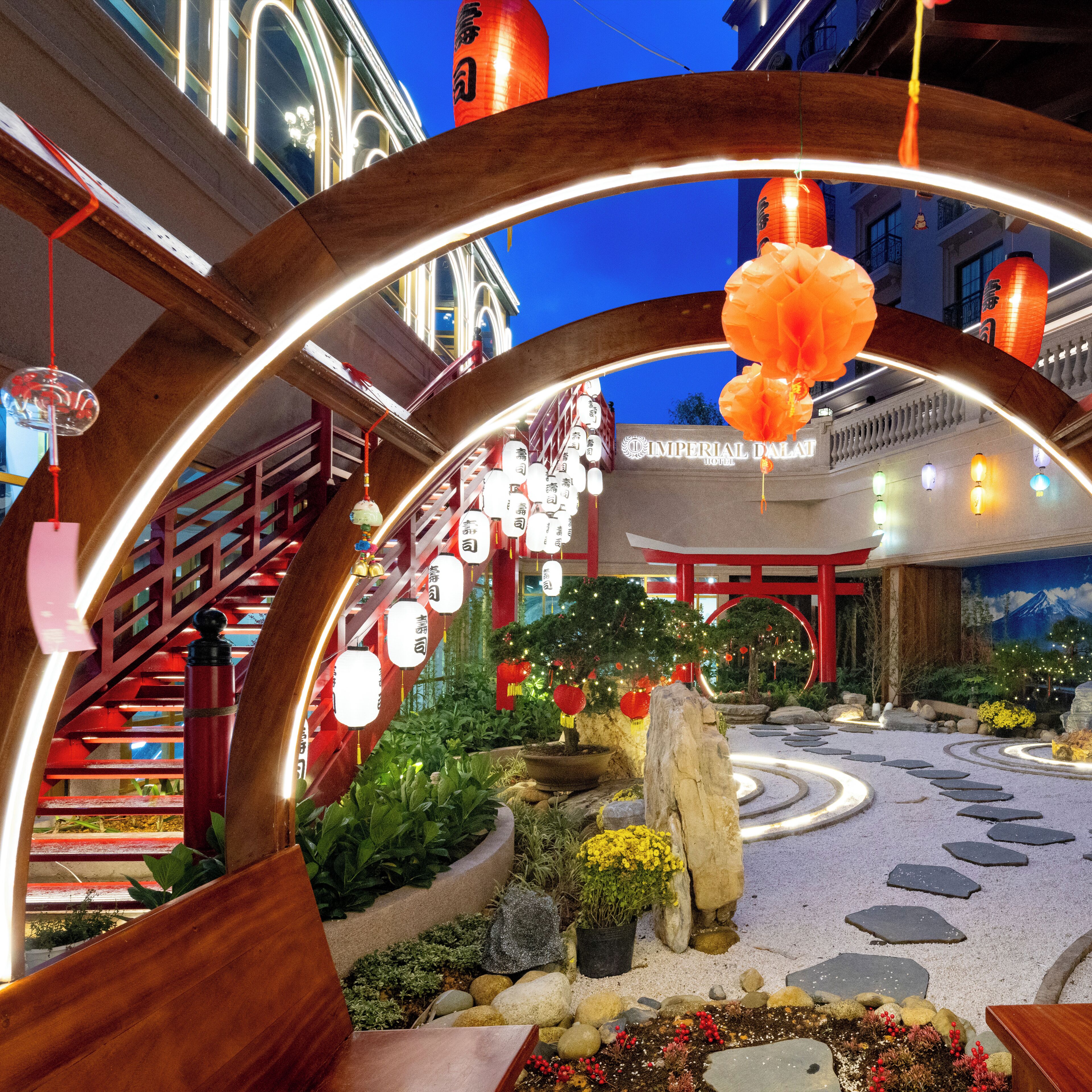 Entrada de hotel con un arco tradicional, una escalera y un jardín con rocas y plantas.