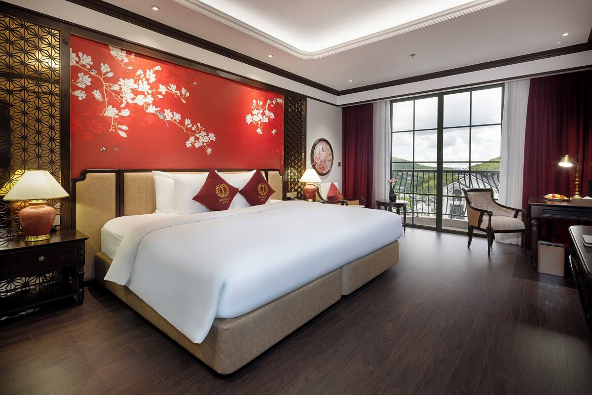 A hotel room with a large bed, a desk, a chair, and a view of the outdoors.