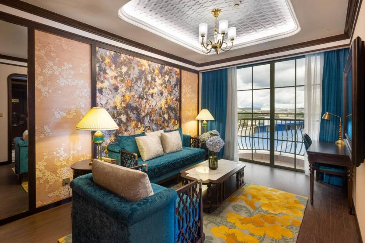 A hotel room with a sofa, two lamps, a table, a view of the sea, and a balcony.