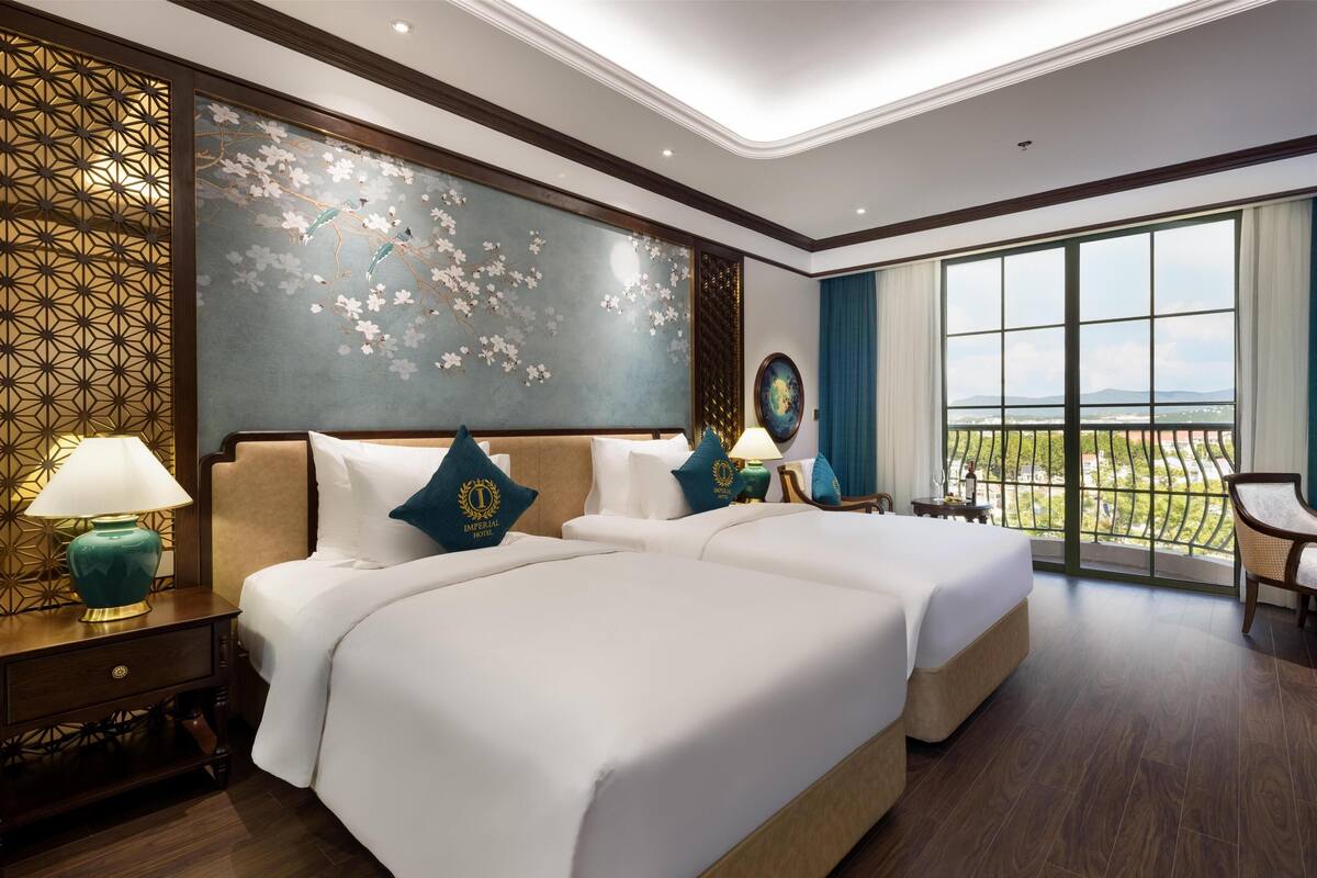 A hotel room with a large bed, two bedside tables, a nightstand, a decorative wall, and a large window with a view.