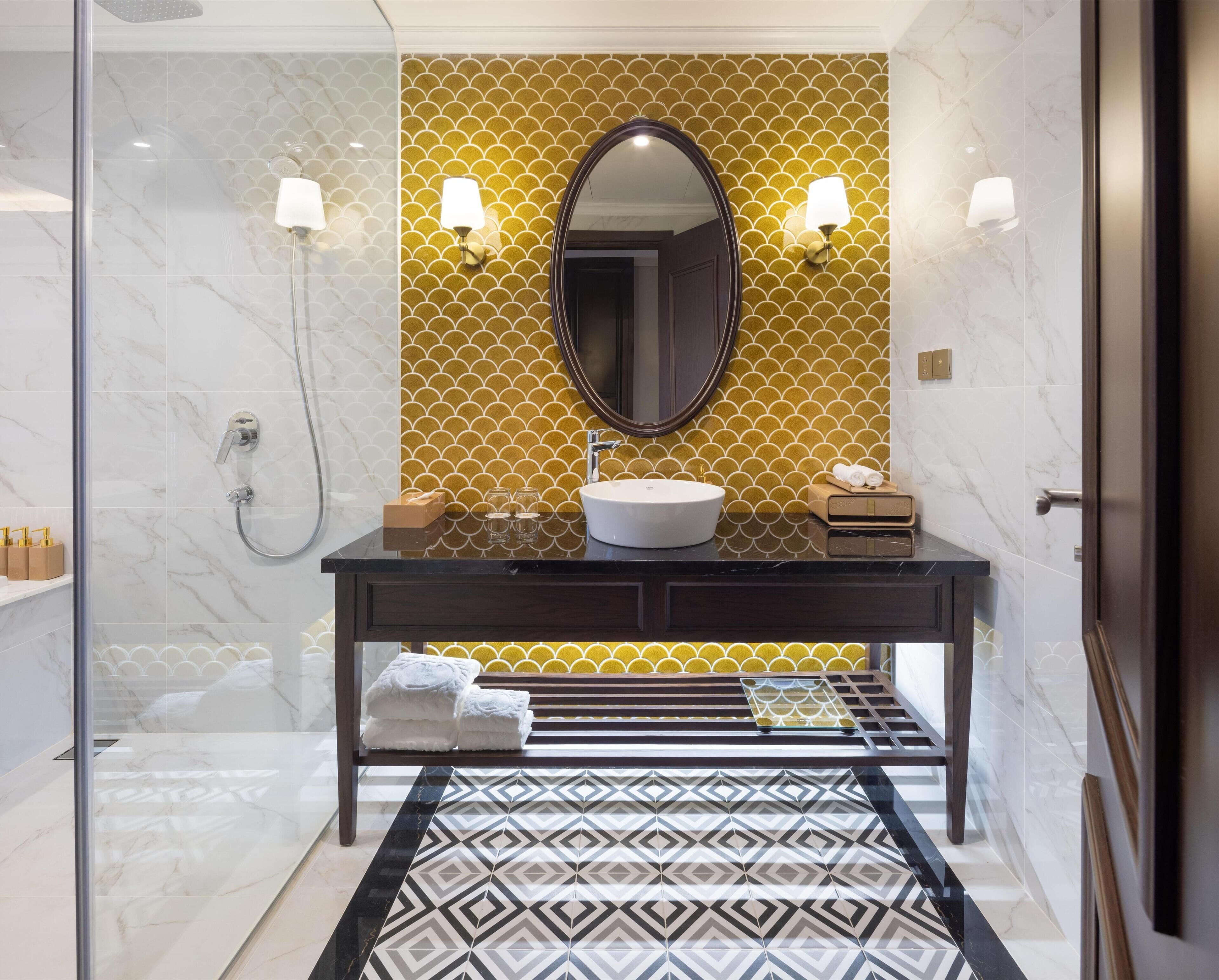 A modern bathroom with a marble floor, a round mirror, a white sink, and a glass-enclosed shower area.