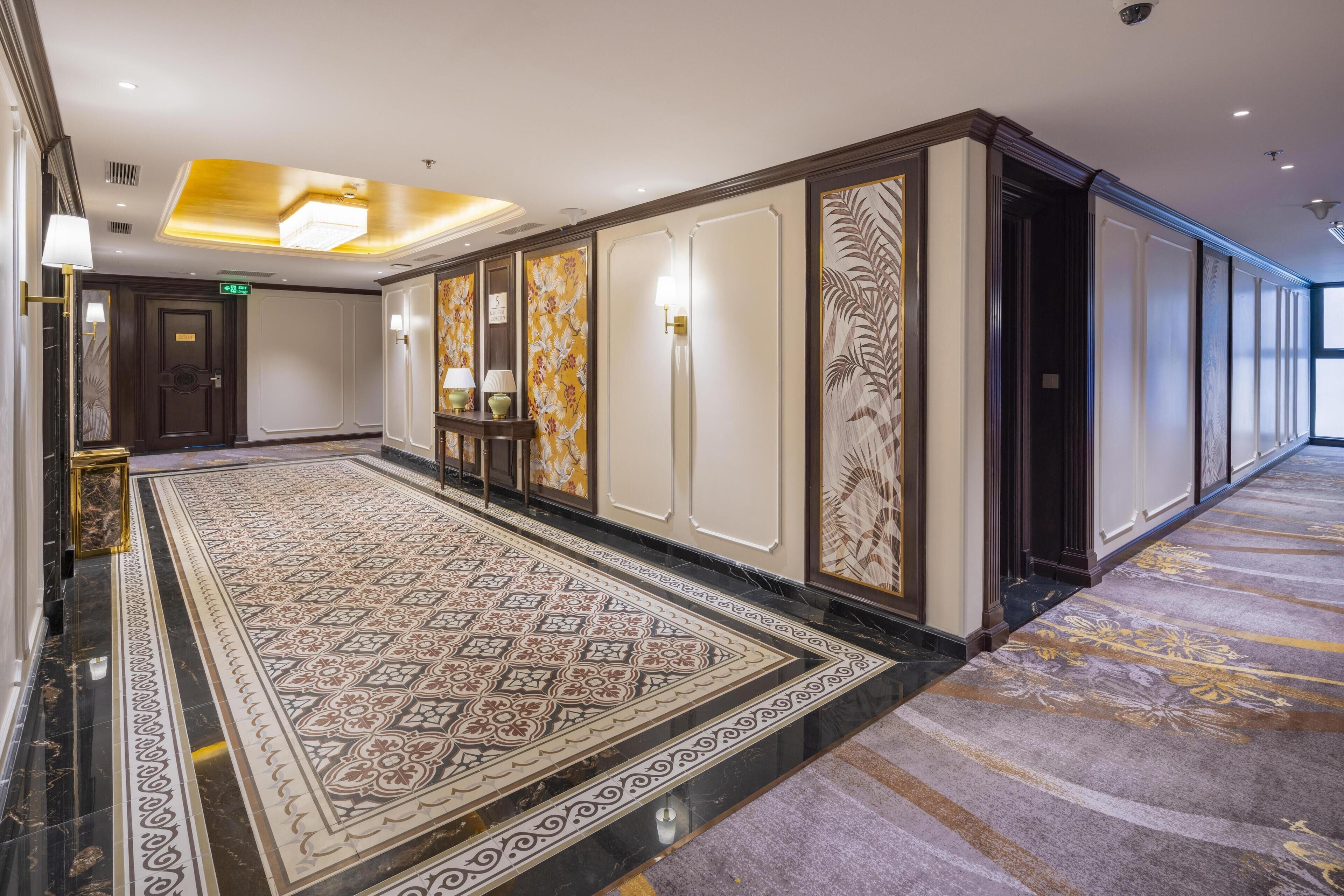 A hotel corridor with a patterned carpet, decorative wall panels, and a marble floor.