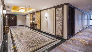 A hotel corridor with a patterned carpet, decorative wall panels, and a marble floor.