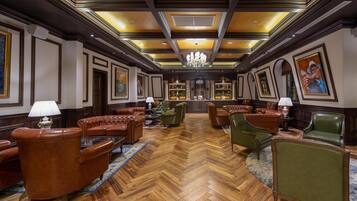 A spacious lobby with leather armchairs, a central coffee table, and a chandelier.