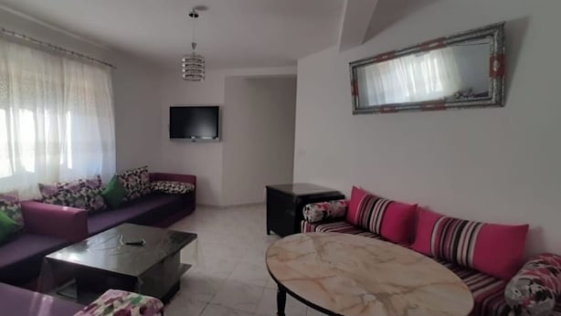 A living room with a sofa set, a coffee table, a TV mounted on the wall, and a small side table. - Tŕés own apartment located in catiér calabonita 5 min from the bus station (Al Hoceïma)