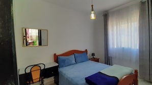 A bedroom with a bed, a desk, a chair, a mirror, and a window with curtains. - Tŕés own apartment located in catiér calabonita 5 min from the bus station (Al Hoceïma)