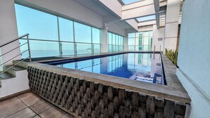 En inomhuspool med väggar av genomskinligt glas, en stenmur och en metalltrappa.