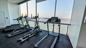 Ett gym med löpband, motionscyklar och en roddmaskin, med utsikt över en sjö eller ett annat vattendrag.