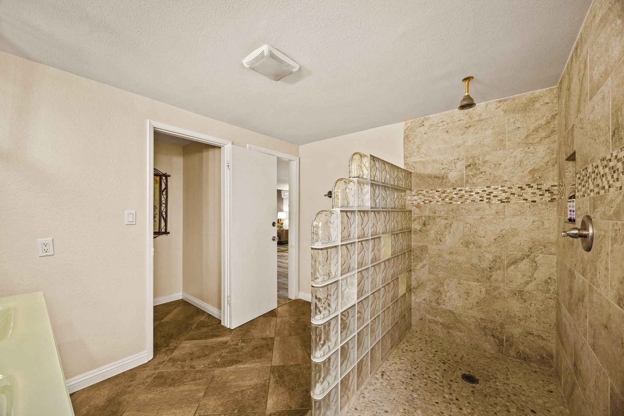 Un bagno con doccia a pavimento, pareti color crema e pavimento piastrellato.