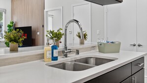 A modern kitchen with a stainless steel sink, white countertops, and wooden paneling on the wall. - Worldcup Ready Stylish 1BR in West Village  Pool + Free Parking (Dallas)