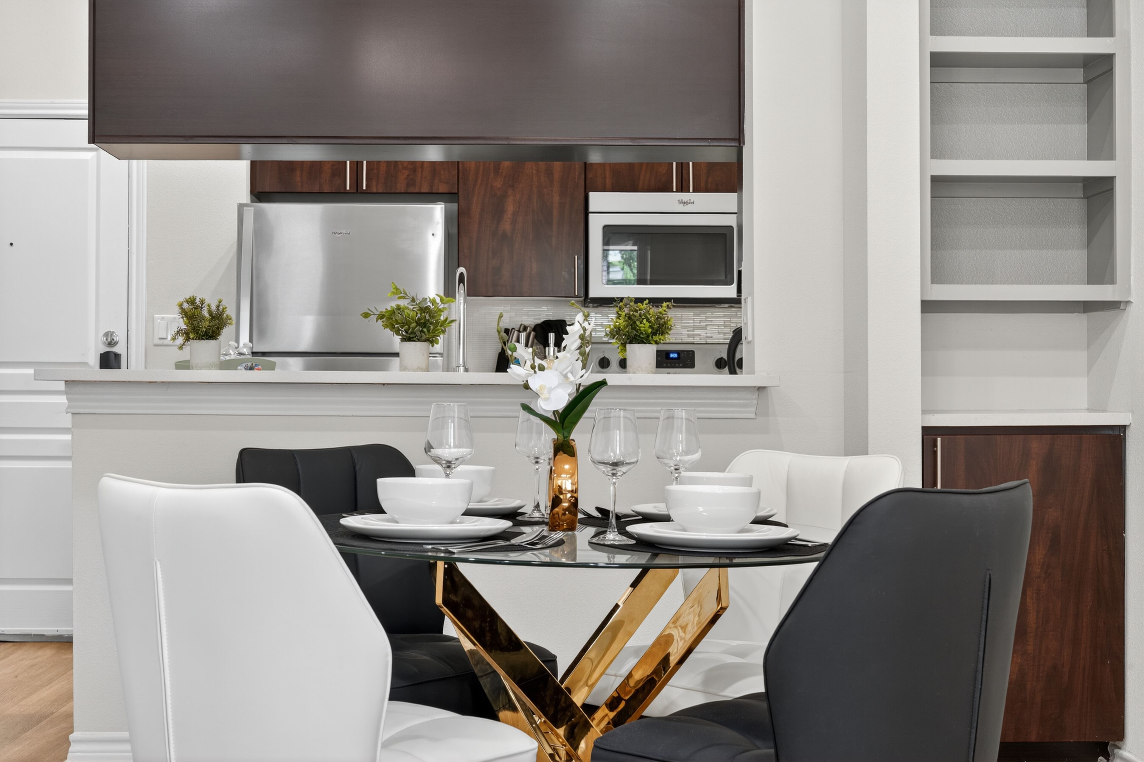 A modern kitchen with stainless steel appliances, a dining area with white chairs, and a central table with a vase of flowers.
