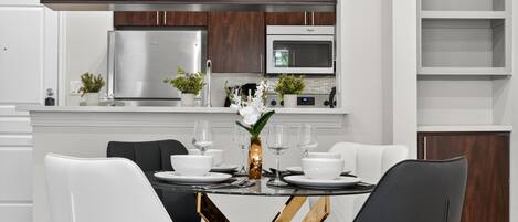 Una cocina moderna con electrodomésticos de acero inoxidable, un comedor con sillas blancas y una mesa central con un jarrón de flores.