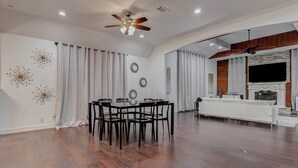 Amplia sala de estar con mesa y sillas de comedor, chimenea y televisor instalado en la pared.