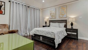 Un dormitorio con una cama grande, dos mesitas de noche con lámparas, una silla y una mesita auxiliar verde.