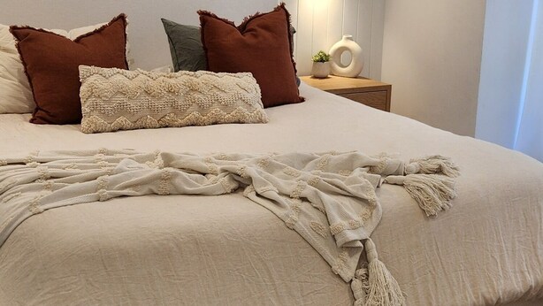 Un dormitorio con una cama grande, un ventilador de techo, una mesita de noche con lámpara y una luz empotrada en la pared.