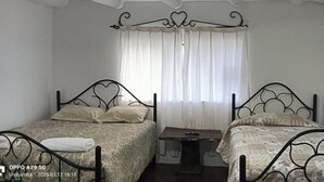 Una stanza con due letti singoli, un tavolino e una finestra con tende.