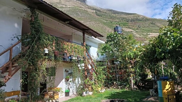 Una casa rustica con un balcone, immersa nel verde e con montagne sullo sfondo.