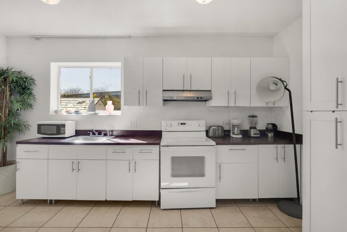 Una cocina moderna con armarios blancos, un microondas, una estufa y una cafetera.