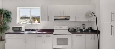 Una cocina moderna con armarios blancos, un microondas, una estufa y una cafetera.