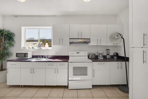 A modern kitchen with white cabinets, a microwave, a stove, and a coffee maker. - Suarez Art Stay, Buena Vista, Sleeps 10, Park (Miami)