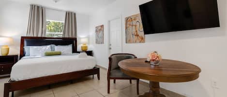 Une chambre d’hôtel avec un lit, une table ronde en bois, une chaise, un téléviseur fixé au mur et des œuvres d’art accrochées aux murs.