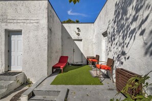 A courtyard with a white wall, a red lounge chair, a small table, and a chair. - Suarez Art Stay, Buena Vista, Sleeps 10, Park (Miami)